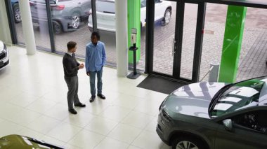 Bir araba satıcısı ve bir müşteri, satış mağazasında araç seçeneklerini tartışır, özellikleri keşfeder ve potansiyel satın alma kararı için fiyatlandırmayı tartışırlar..