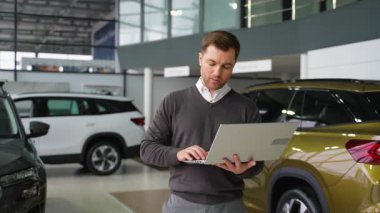 Profesyonel bir araba satıcısı galeride dizüstü bilgisayar kullanır, araç verilerini analiz eder, envanteri kontrol eder ve müşteri bilgilerini yönetir..