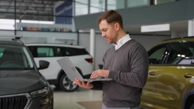 Profesyonel bir araba satıcısı, modern bir galeride araba envanterini, hipodrom satışlarını ve araba kullanımını kontrol etmek için dizüstü bilgisayar kullanır..