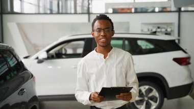 Beyaz tişörtlü profesyonel bir araba satıcısı modern bir galeride müşterilere araç soruşturmaları ve satışlarında yardımcı olmaya hazır..