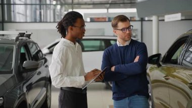 Afrikalı Amerikalı bir araba satıcısı, potansiyel bir alıcıya, modern bir galeride Kara Cuma günü satış etkinliği sırasında araç seçmesinde yardım ediyor..