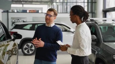 Afrikalı Amerikalı bir araba satıcısı, modern bir galeride potansiyel bir alıcıyla indirimli bir teklif tartışıyor ve ona en iyi anlaşmayı seçmesinde yardımcı oluyor..