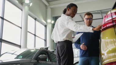Bir Afro-Amerikalı araba satıcısı, yeni bir SUV 'nin özelliklerini satış mağazasındaki bir müşteriye açıklar ve satın alma kararına yardımcı olur..