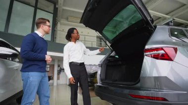 Bir araba satıcısı bir galeri içerisindeki bir müşteriye kargo alanı ve araç özelliklerinin altını çizerek satın almadan önce bir SUV 'nin bagaj kapasitesini açıklar..