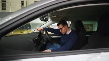 Düşünceli bir adam sağ elini kullanan bir arabada oturur, torpidoyu dikkatle inceler ve son satın alma kararını vermeden önce kontrol eder..