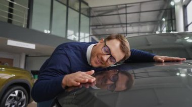 Neşeli bir adam yeni arabasının kaputunu kucaklıyor, galeriden hayalindeki aracı aldıktan sonra mutluluk ve heyecanı ifade ediyor..