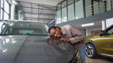 Mutlu bir adam galeride yeni arabasının kaputuna sarılıyor. Son aldığı araçtan duyduğu neşe ve heyecanı dile getiriyor..