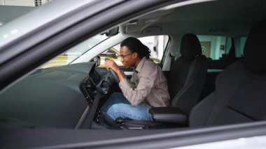 Afro-Amerikalı bir adam yeni aldığı sağ ön sürücü arabasında oturuyor, galerideki indirimli satış anlaşması için heyecanlı..