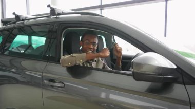 Mutlu bir Afrikalı Amerikalı adam, yeni aldığı sağ şeritli arabasında oturuyor, gülümsüyor ve elinde modern bir galerinin anahtarlarını tutuyor..