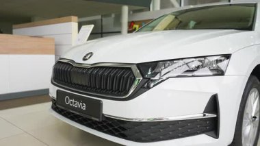 Bir galeride beyaz bir Skoda Octavia 'nın yakın çekimi. Modern sedan parlak bir ön ızgara, LED farlar ve şık bir tasarım içerir..
