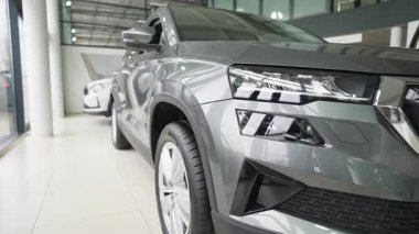 Modern bir araba galerisinde sergilenen parlak, metalik gri bir SUV. Yakın çekimde LED farlar, ön ızgara ve premium tasarım ayrıntıları vurgulanıyor.