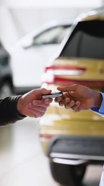 Bir araba satıcısı, yeni bir aracın anahtarlarını teslim ederken müşterisiyle tokalaşıyor ve modern bir galeride satışını tamamlıyor..