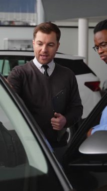 Bir araba satıcısı, bir galerideki potansiyel alıcıya bir aracın özelliklerini açıklar ve karar verme sürecine yardımcı olur..