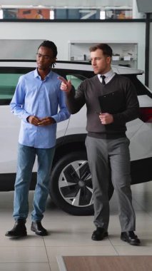 Bir araba satıcısı, bir galeride Afrikalı Amerikalı bir müşteriyle indirimli bir araç anlaşmasını tartışıyor. Doğru arabayı seçmesine ve satın almayı sonuçlandırmasına yardım ediyor..