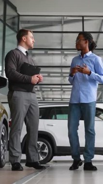 Araba satıcısı müşteriye galeride araç seçmesinde yardımcı olur. Potansiyel alımlar için özellikler, fiyatlandırma ve finansman seçeneklerini tartışır..