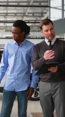 Bir araba satıcısı, Afro-Amerikalı bir müşteriye galeride araç seçmesinde yardımcı olur. Satın almadan önce özellikleri, fiyatları ve finansman seçeneklerini tartışır..