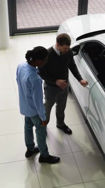 Bir araba satıcısı, satış mağazasında potansiyel bir alıcıya beyaz bir SUV sunar. Satın alma kararı için tasarımını ve özelliklerini vurgular..