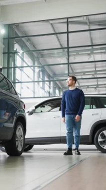 Şık bir adam parlak bir araba galerisinde yürüyor, çeşitli araçları keşfediyor ve bir galeriden yeni bir şey almak için seçenekleri değerlendiriyor..