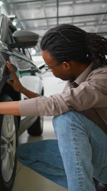 Odaklanmış Afro-Amerikalı bir adam, satın almadan önce modern bir galeride yeni bir arabanın dış ve arka tamponunu yakından inceliyor..