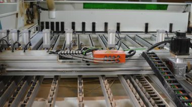 Modern bir mobilya üretim tesisinde ahşap işçiliği için kullanılan otomatik CNC makinesinin ayrıntılı görüntüsü. Endüstriyel kablolar, çalıştırıcılar ve raylar görünür..