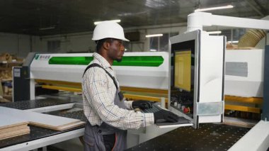Fabrika işçisi, lamine ahşap tahtaları mobilya parçalarına ayırmak için CNC testeresi kullanıyor. Modern bir üretim atölyesinde dijital kontrollere odaklanmış..