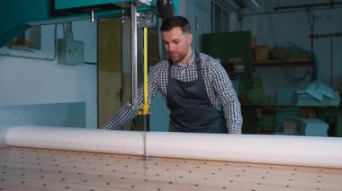 Dikey bant kullanan bir adam atölye ortamında koruyucu önlük giymiş ve odaklanmış beyaz köpük kauçuk kesmek için testere kullanıyor..