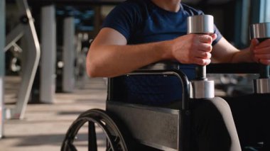 Tekerlekli sandalyedeki bir adamın spor yaparken dambılları kavraması, dayanıklılık, zindelik ve adaptasyon eğitimini temsil etmesi..