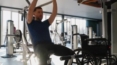 Engelli bir atletizm sporcusu spor salonunda son sürat egzersiz yapıyor. Tekerlekli sandalye yanında, dayanıklılık ve vücut kondisyonuna odaklanmış..