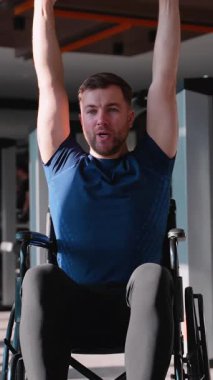 Tekerlekli sandalyedeki adam spor salonunda dambılları kaldırıyor, üst vücut gücüne, adaptasyon eğitimine ve kişisel yetkilendirmeye odaklanıyor..