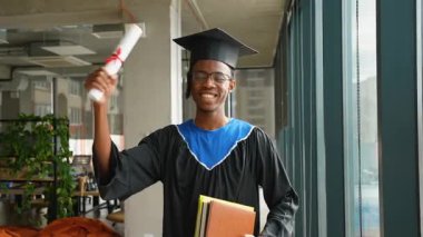 Şapka ve cübbeyle gülümseyen Afrikalı Amerikalı mezunlar, parlak, modern bir akademik alanda dururken gururla diploma ve kitap tutarlar..