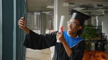 Şapka ve cübbe giymiş neşeli Afrikalı Amerikalı mezunlar, aileleriyle telefon görüşmeleri yaparken başarılarını kutluyor, diplomalarını gururla taşıyorlar..