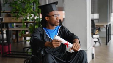 Mezuniyet kepi ve cüppeli dalgın Afrikalı öğrenci tekerlekli sandalyede oturuyor, diplomasını tutuyor ve akademik başarılarını yansıtıyor..