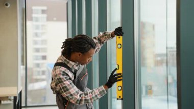 Modern bir ofis veya bina içinde büyük bir cam pencere kurmak ve hizalamak için ruh seviyesini kullanan yetenekli bir inşaat işçisi..