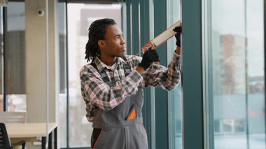 Odaklanmış Afrikalı Amerikalı işçiler, modern bir ticari bina içerisindeki montaj çalışmaları sırasında bir kabartma tabancası kullanarak pencere çerçevesine dolgu macunu sürerler..