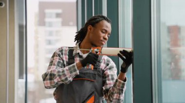 Odaklanmış inşaat işçisi, yalıtım için pencere kenarlarına köpük dolgu maddesi ve ofiste uygun pencere kurulumu uygulamak için kazıma tabancası kullanır.