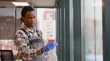 İş üniformalı ve eldivenli bir hademe modern ticari ofis ortamında uzun bir pencereyi temizlemek için bir cam sileceği kullanır..