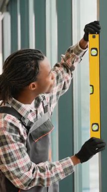Modern bir ofis veya bina içinde büyük bir cam pencere kurmak ve hizalamak için ruh seviyesini kullanan yetenekli bir inşaat işçisi..