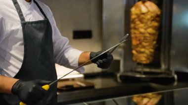 Şefin ellerinin detaylı bir şekilde keskinleştirilmiş bir bıçakla arka planda dönen bir shawarma eti..