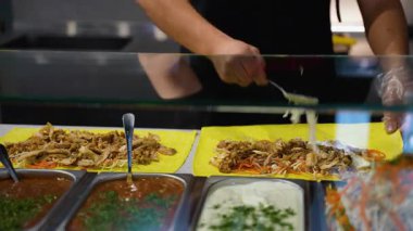 Shawarma paketleri hazırlayan eller, hazır et, sebze ve beyaz sos ile fast food tezgahında taze malzemelerle birlikte..