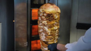 Sulu shawarma et yığınının yakın plan çekimi. Profesyonel mutfak ortamında şefin elinde ahşap spatulayla dikey rostoda kızartılıyor..