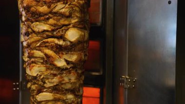Ticari bir mutfak ortamında düşey bir rostoda kızartılan sulu, altın sarısı shawarma etinin ayrıntılı görüntüsü.