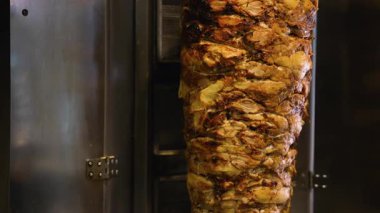Ticari bir mutfak ortamında düşey bir rostoda kızartılan sulu, altın sarısı shawarma etinin ayrıntılı görüntüsü.