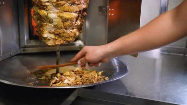Taze oyulmuş shawarma eti, bir el onu ahşap bir spatulayla alıp ticari mutfakta bir tepsiye koyarken dönüşümlü tükürükten düşer..