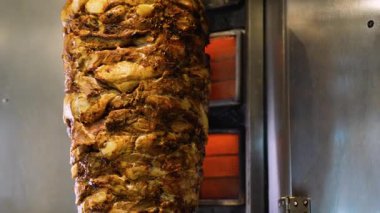Kıtır kıtır, terbiye edilmiş shawarma etinin arka planda parlayan ısı elementleriyle birlikte dikey bir rostoda kızarmasının ayrıntılı görüntüsü..