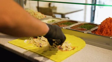 Biftek hazırlayan bir şefin yakın plan resmi. Sarı lahana, havuç, otlar ve sosla birlikte bir yemek tezgahında..