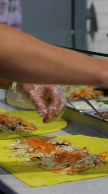 Hazır yemek reyonunda diyet dostu shawarma ve taze sebzeler için sarı tortilla üzerine sos döken şefin yakın çekimi..