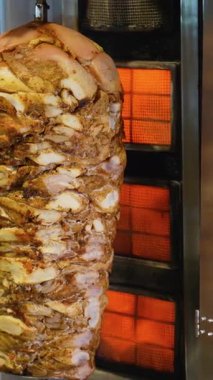 Büyük bir yığın baharatlı shawarma eti dikey ızgarada pişiyor ve şefin elinde ahşap bir spatula var..