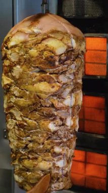 Büyük bir yığın baharatlı shawarma eti dikey ızgarada pişiyor ve şefin elinde ahşap bir spatula var..