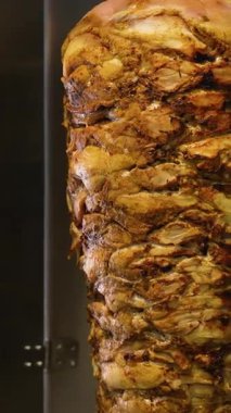 Ticari bir mutfak ortamında düşey bir rostoda kızartılan sulu, altın sarısı shawarma etinin ayrıntılı görüntüsü.