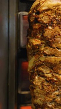 Baharatlı shawarma et yığınının yakın çekimi dikey ızgarada kızartılıyor, çıtır çıtır ve zengin dokuları gösteriyor..